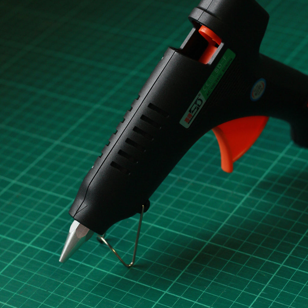 A black hot glue gun with an orange trigger and silver metal tip.