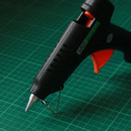 A black hot glue gun with an orange trigger and silver metal tip.